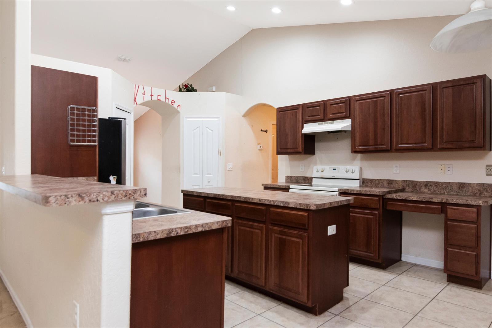 A kitchen features dark wood cabinets, laminate countertops, a central island, and tile flooring — 12276 N Villa Road, Spring Hill FL 34609, SPRING HILL, FL