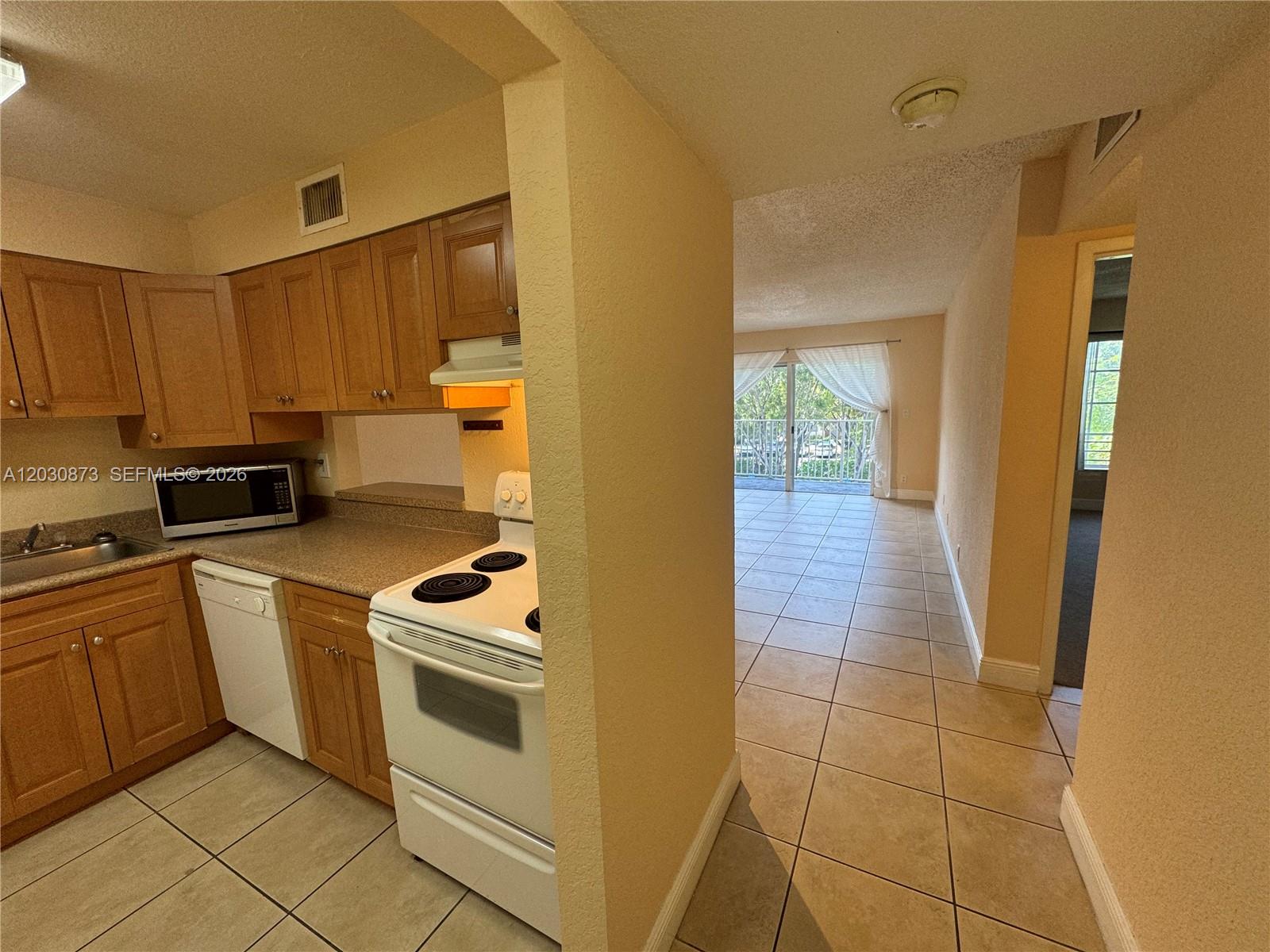 A kitchen with wood cabinets and white appliances opens into a tiled living area — 5201 Geneva Way # 308, Doral FL 33166, DORAL, FL