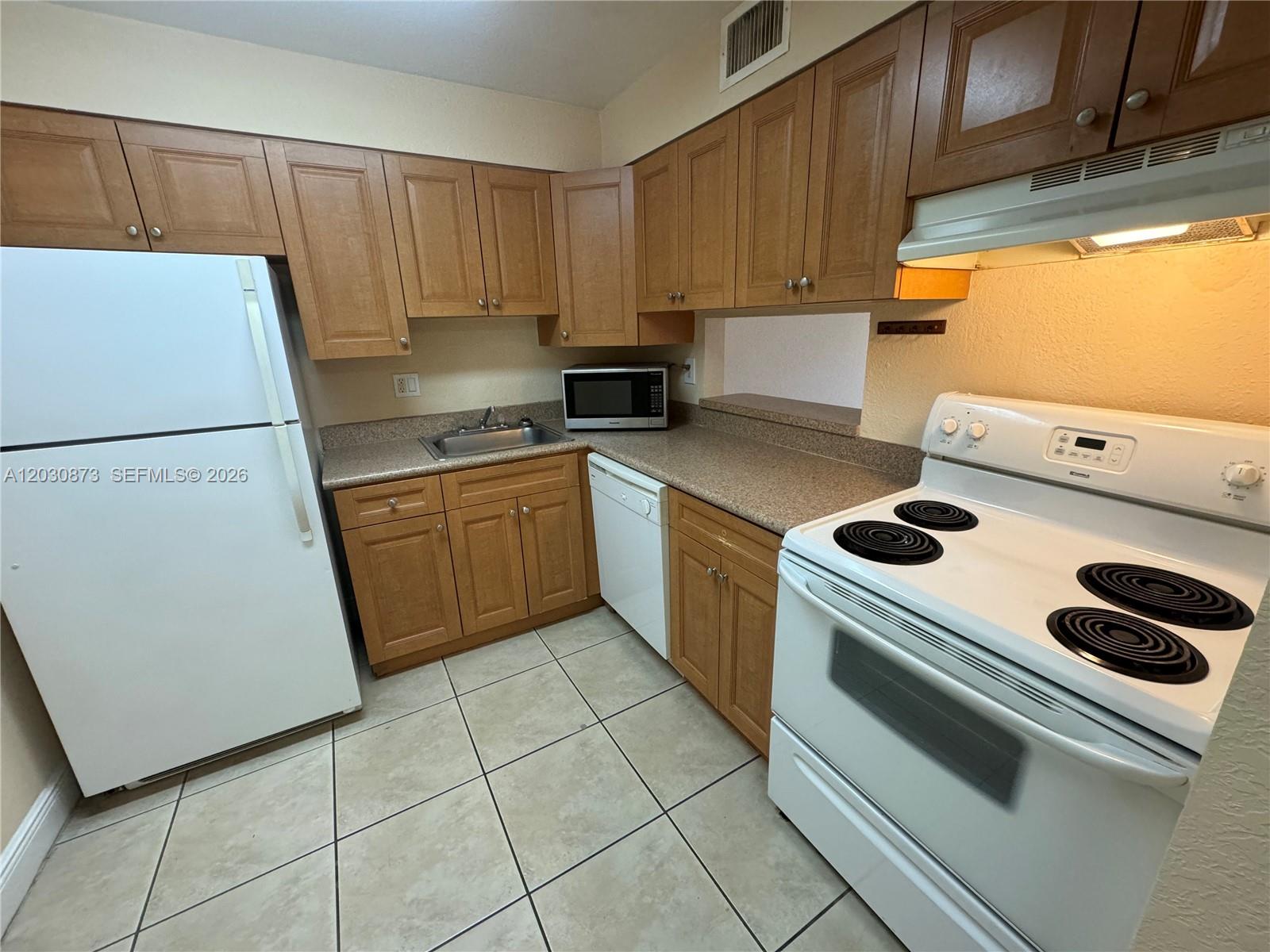 A kitchen features wood cabinets, white appliances, tan countertops, and light-colored tile flooring — 5201 Geneva Way # 308, Doral FL 33166, DORAL, FL