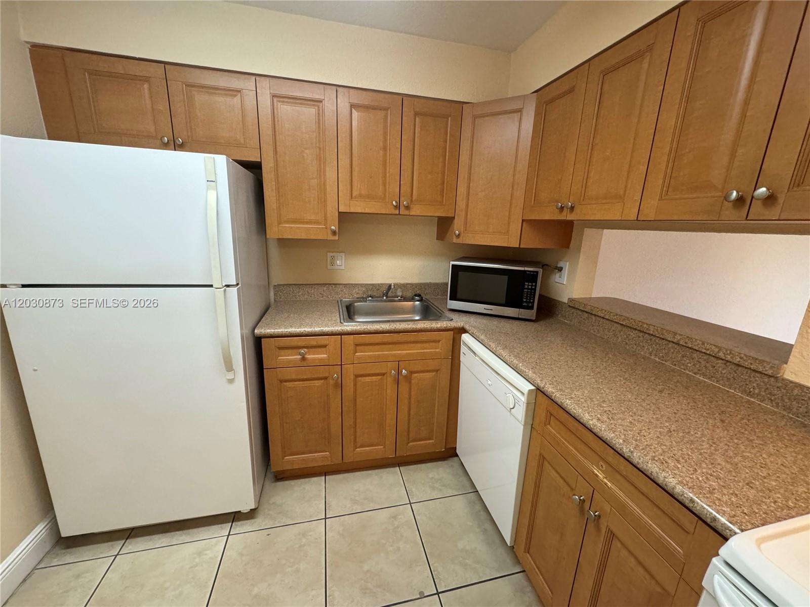 A kitchen features wood cabinets, tan laminate countertops, a white refrigerator, and a white dishwasher — 5201 Geneva Way # 308, Doral FL 33166, DORAL, FL