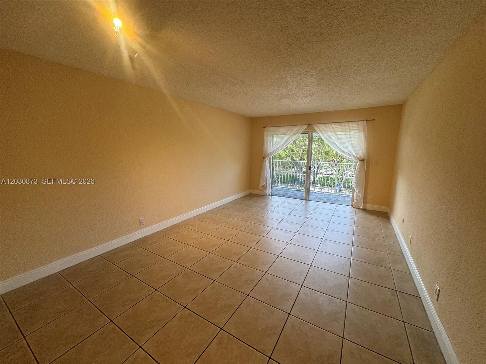 An empty room features tan walls, tiled flooring, and a sliding glass door to a balcony — 5201 Geneva Way # 308, Doral FL 33166, DORAL, FL