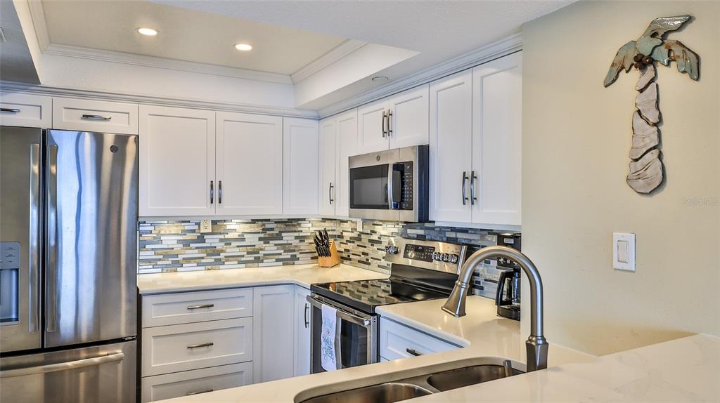A kitchen features white cabinets, stainless steel appliances, a mosaic tile backsplash, and quartz countertops — 5207 S ATLANTIC AVENUE UNIT 1226, NEW SMYRNA BEACH, FL