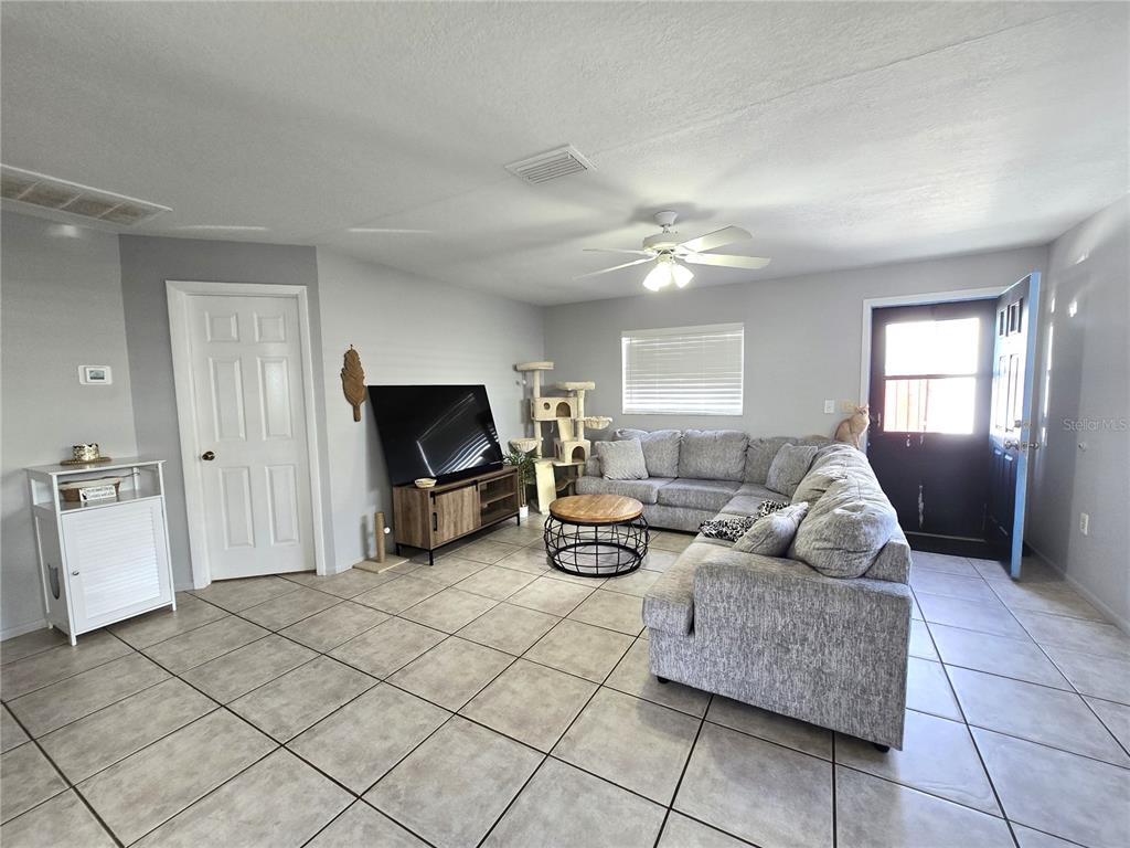 A living room features light gray walls, tile flooring, a sectional sofa, and a television — 5422 AMY LANE, NEW PORT RICHEY, FL