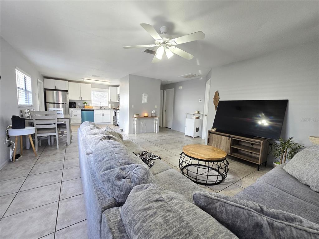 An open-concept living room and kitchen featuring tile flooring, a large sectional, and ceiling fan — 5422 AMY LANE, NEW PORT RICHEY, FL