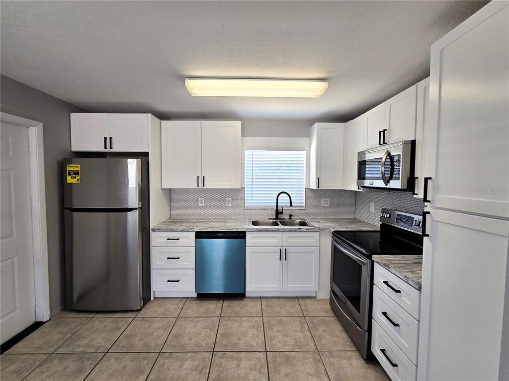 A kitchen features white cabinets, stainless steel appliances, a tiled backsplash, and light-colored floor tiles — 5422 AMY LANE, NEW PORT RICHEY, FL