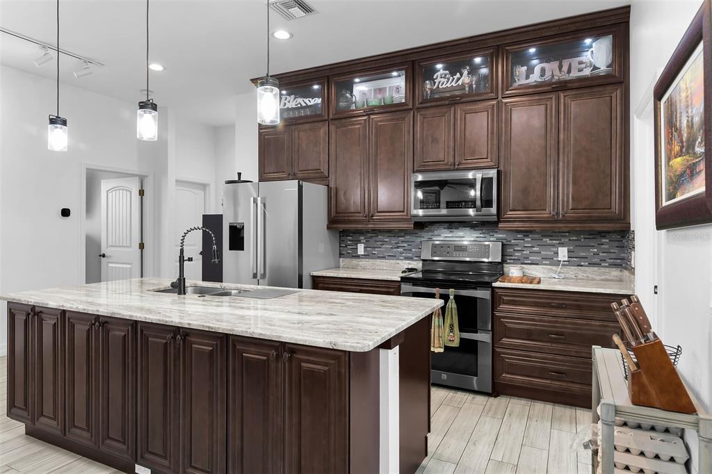 A kitchen features dark wood cabinets, a large stone-topped island, and stainless steel appliances — 40200 LITTLE FARM ROAD, PUNTA GORDA, FL