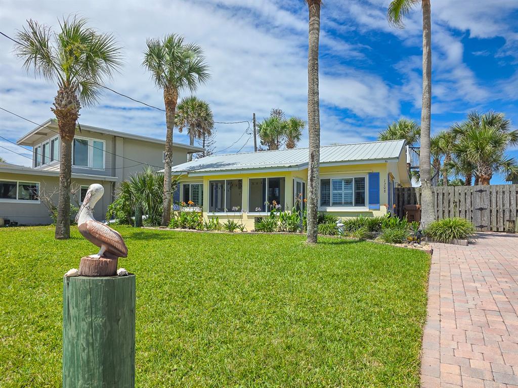 A yellow single-story house with a metal roof sits behind a lawn with a pelican statue — 1208 S CENTRAL AVENUE, FLAGLER BEACH, FL