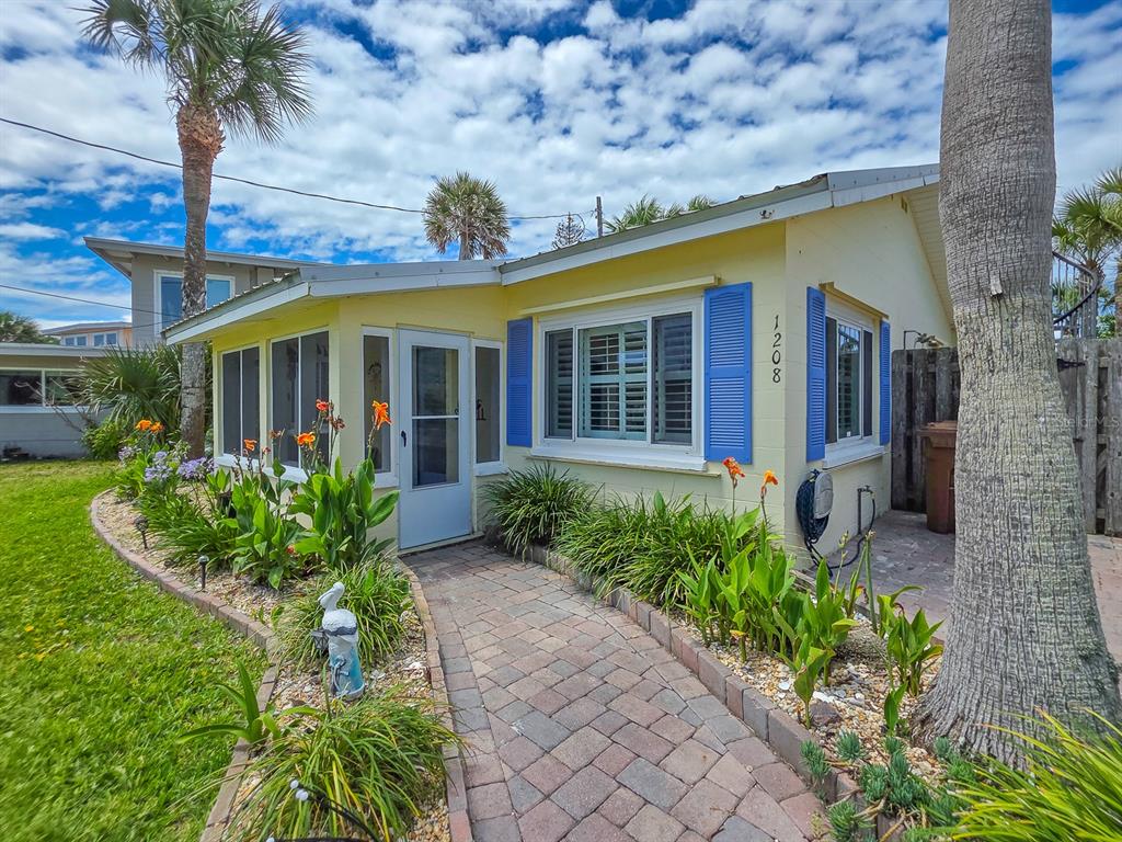 A yellow house with blue shutters features a brick walkway leading to the front door — 1208 S CENTRAL AVENUE, FLAGLER BEACH, FL