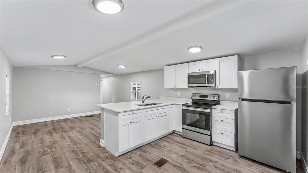 A kitchen with white cabinets, stainless steel appliances, and wood-look flooring in an open space — 212 KAYLOR DRIVE, AUBURNDALE, FL