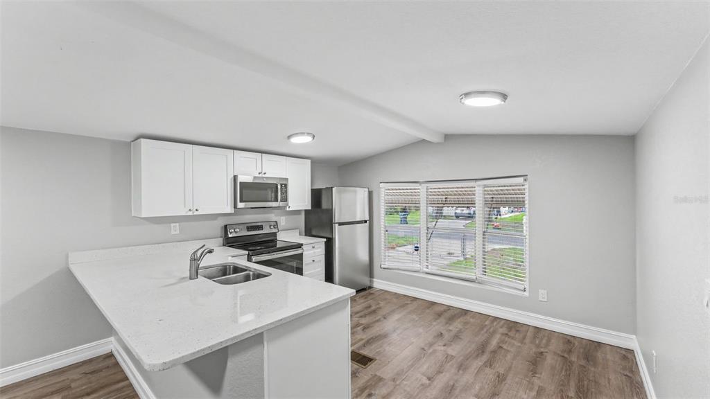 A kitchen features white cabinetry, stainless steel appliances, a quartz countertop, and wood-look flooring — 212 KAYLOR DRIVE, AUBURNDALE, FL