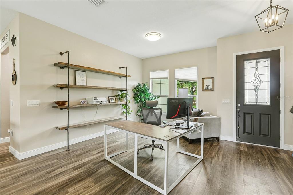 A home office features wood-look flooring, industrial-style shelving, a desk, and a dark front door — 9876 PANGOLA LOOP, LAND O LAKES, FL
