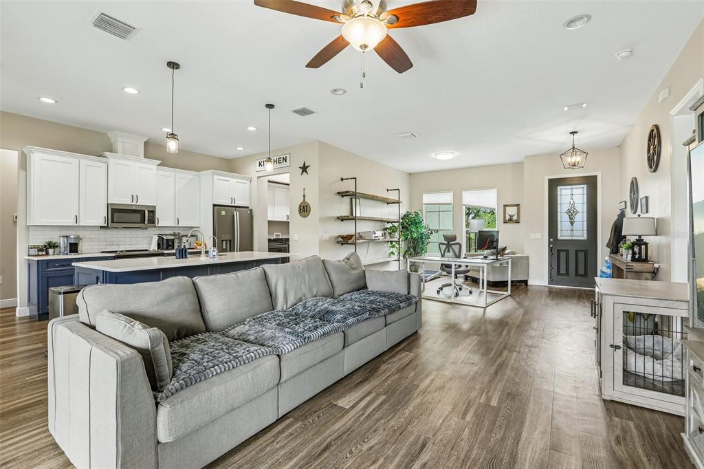 An open-concept living area features a gray sofa, kitchen with island, and a home office — 9876 PANGOLA LOOP, LAND O LAKES, FL