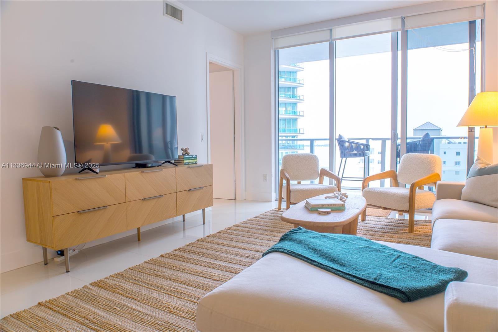 A bright living room features a wooden media console, two armchairs, and a balcony view — 1300 Brickell Bay Dr # 1608, Miami FL 33131, MIAMI, FL