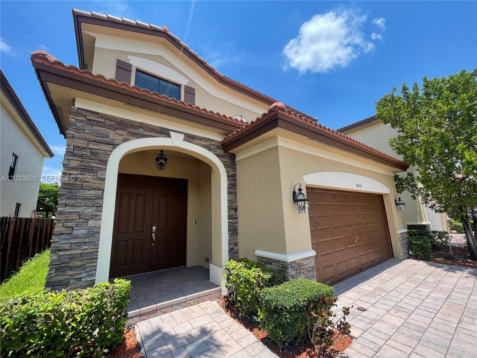 A two-story house exterior features a stone facade, a tiled roof, and a paved driveway — 8858 NW 101st Pl, Doral FL 33178, DORAL, FL