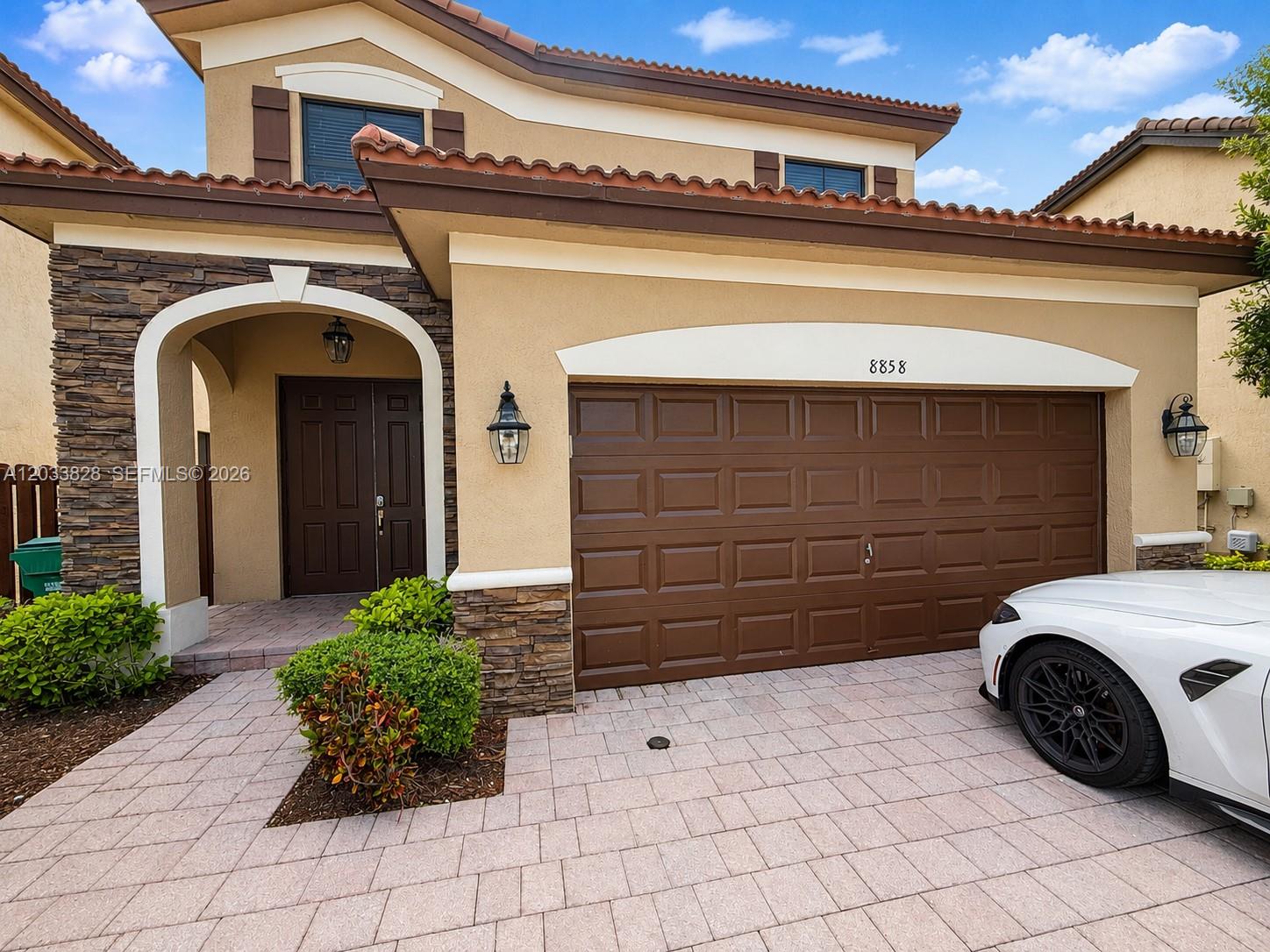 The exterior of a two-story house features a stone-accented entryway, brown garage door, and driveway — 8858 NW 101st Pl, Doral FL 33178, DORAL, FL