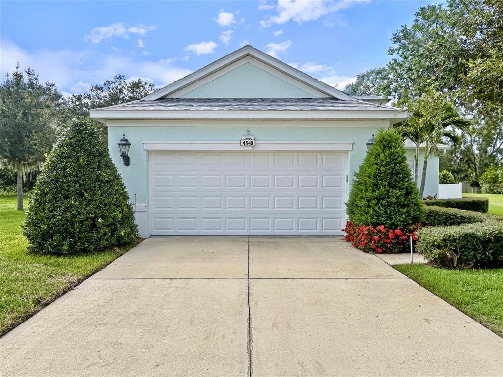 A light green house features a two-car garage and manicured landscaping under a blue sky — 4548 29TH AVENUE CIRCLE E, PALMETTO, FL