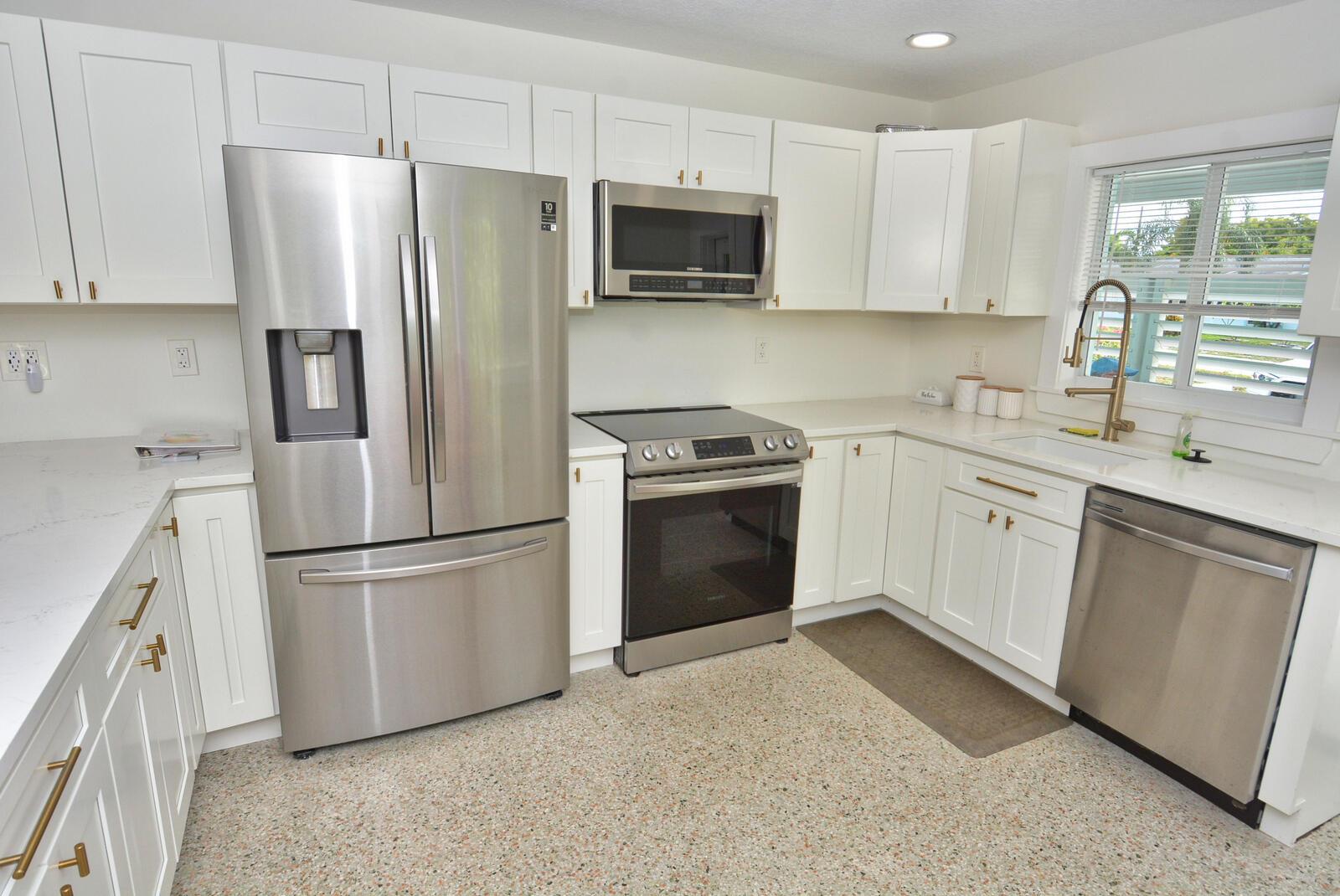A kitchen features white cabinets, stainless steel appliances, quartz countertops, and a terrazzo floor — 1395 NE Flora Place, Jensen Beach FL 34957, JENSEN BEACH, FL
