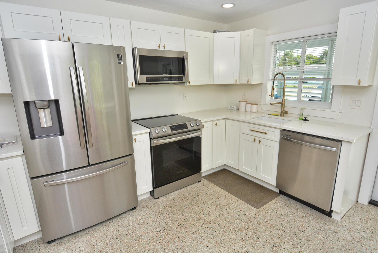 A kitchen with white cabinets, stainless steel appliances, and a speckled floor — 1395 NE Flora Place, Jensen Beach FL 34957, JENSEN BEACH, FL