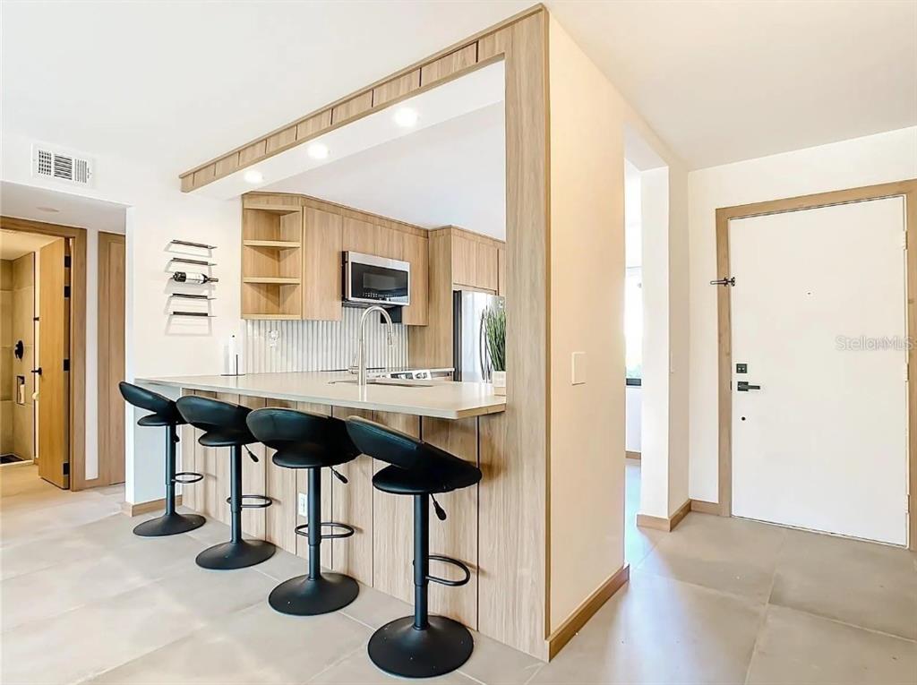 A kitchen features light wood cabinetry, a breakfast bar with four stools, and tile flooring — 5532 PUERTA DEL SOL BOULEVARD S UNIT 136, ST PETERSBURG, FL