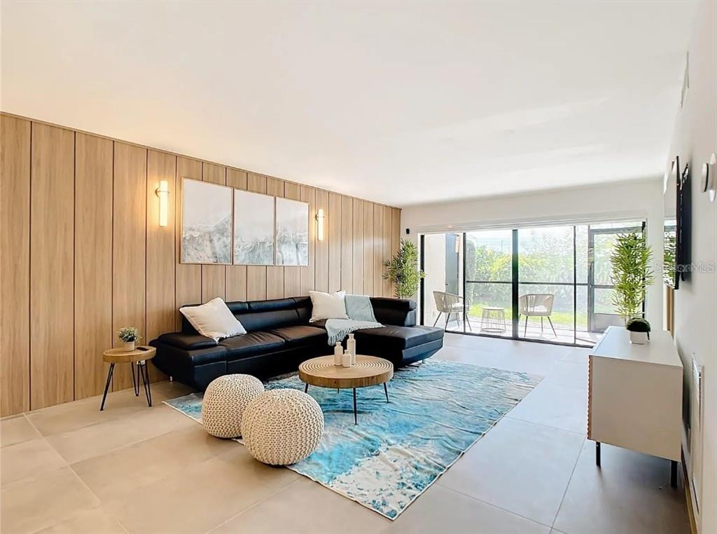 A living room features wood-paneled walls, a black sectional sofa, and a blue area rug — 5532 PUERTA DEL SOL BOULEVARD S UNIT 136, ST PETERSBURG, FL