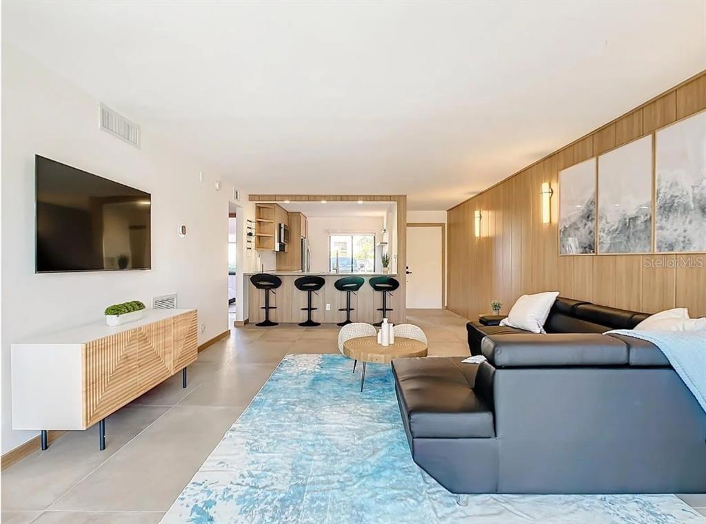 A living room with a black sectional sofa, blue area rug, and kitchen breakfast bar — 5532 PUERTA DEL SOL BOULEVARD S UNIT 136, ST PETERSBURG, FL