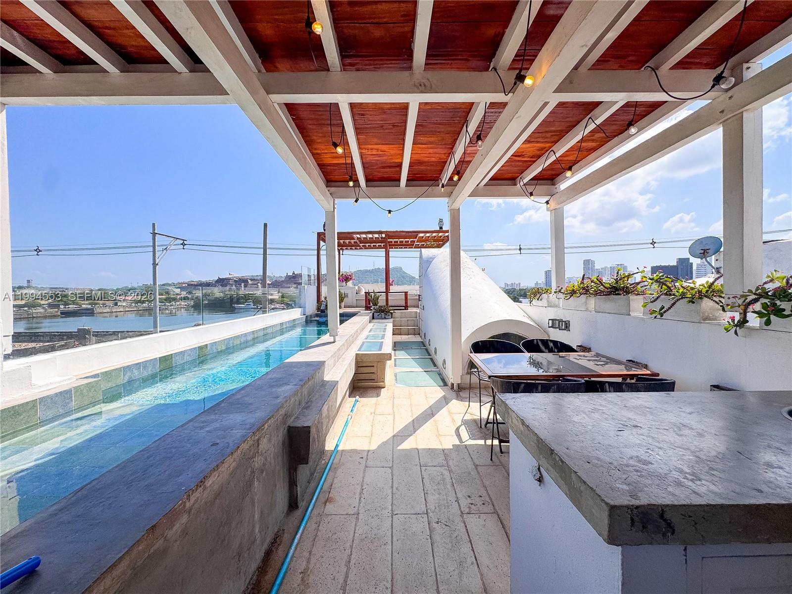 A rooftop terrace features a long lap pool, a dining area, and a wooden pergola — El Pedregal Cartagena, Colombia, OU 0, OU