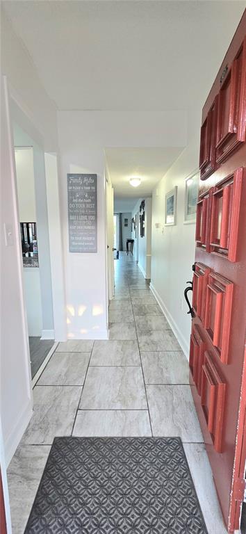 A view from an open red front door into a hallway with light-colored tile flooring — 1012 PEARCE DRIVE UNIT 307, CLEARWATER, FL