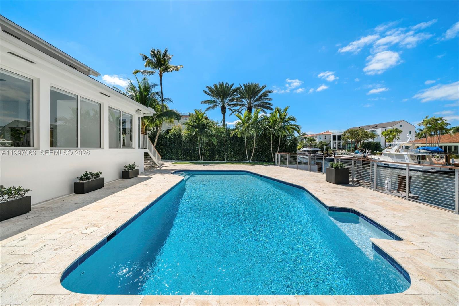 A rectangular swimming pool sits on a stone patio beside a white house and canal — 6832 Sunrise Ct # 0, Coral Gables FL 33133, CORAL GABLES, FL