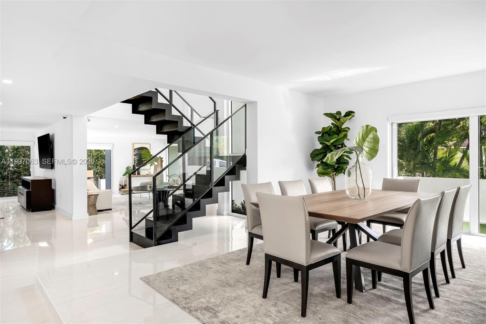 A modern dining room features a wooden table, grey chairs, and a floating staircase — 6832 Sunrise Ct # 0, Coral Gables FL 33133, CORAL GABLES, FL