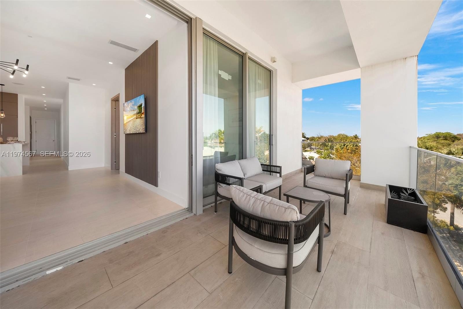 A balcony with outdoor seating overlooks a landscape through a glass railing — 246 NE 6th Ave # 302, Delray Beach FL 33483, DELRAY BEACH, FL