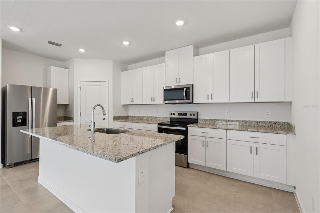 A kitchen featuring white cabinets, granite countertops, stainless steel appliances, and a central island — 78 WANDERING CREEK WAY, PALM COAST, FL