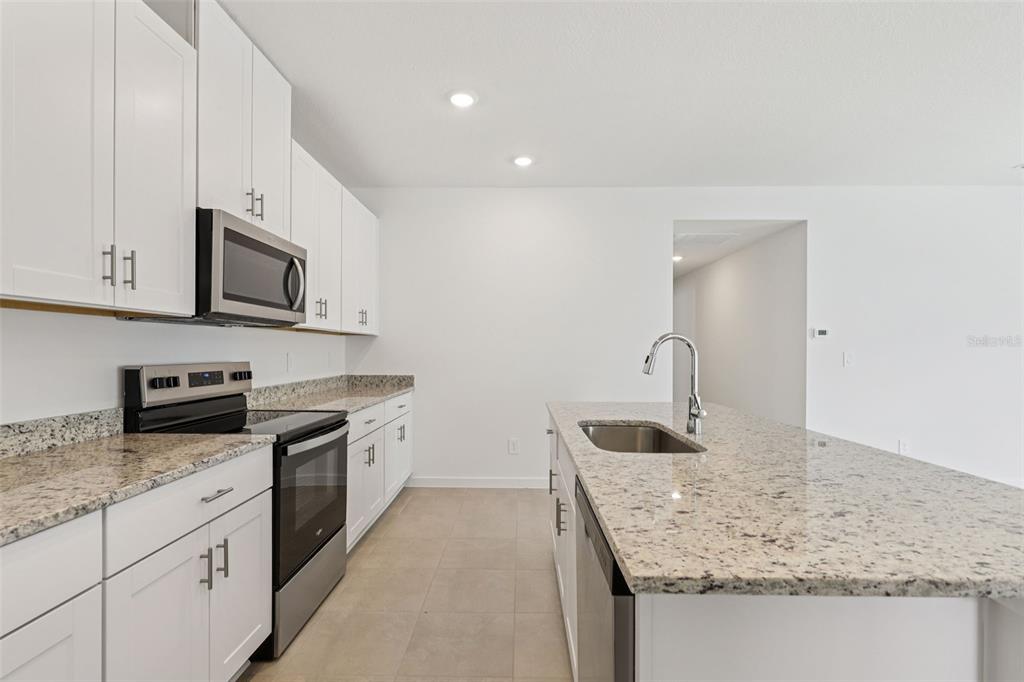 A kitchen features white cabinets, granite countertops, stainless steel appliances, and a central island — 78 WANDERING CREEK WAY, PALM COAST, FL