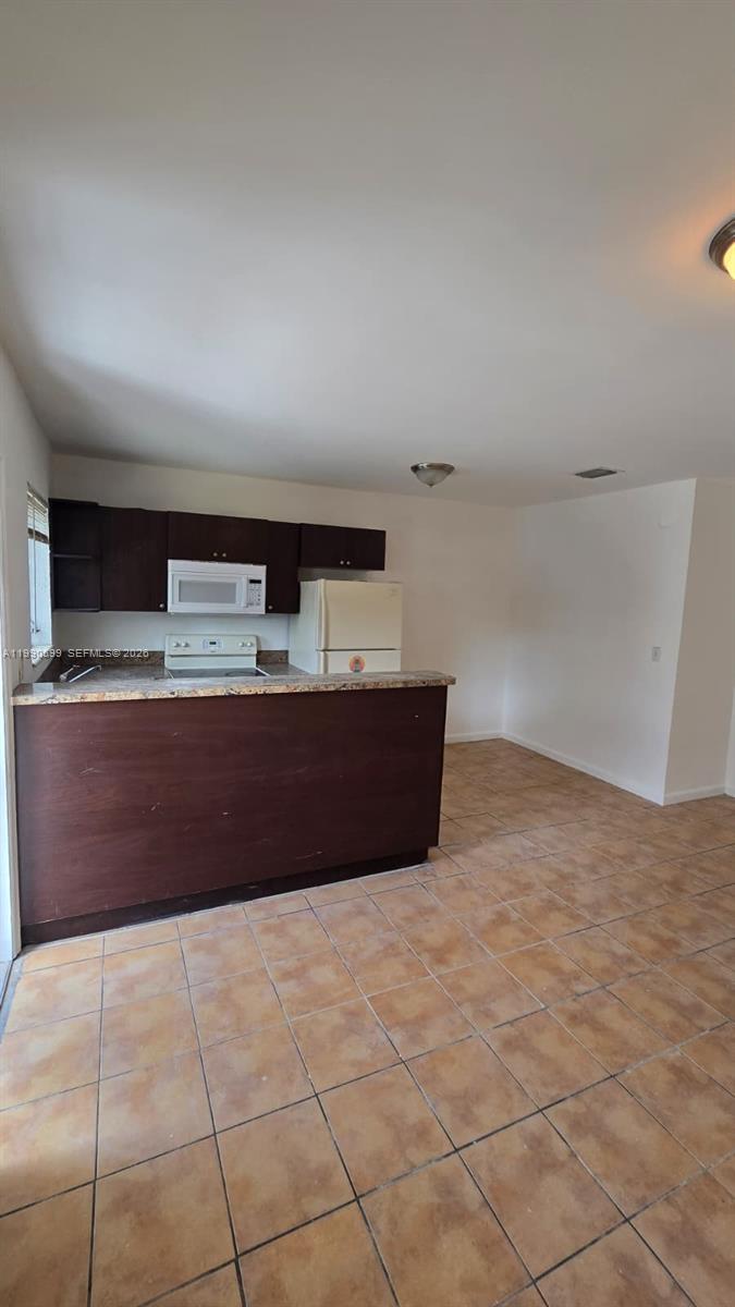 A kitchen features dark wood cabinets, a white microwave, a refrigerator, and tiled flooring — 16131 NE 19th Pl # 3, North Miami Beach FL 33162, NORTH MIAMI BEACH, FL