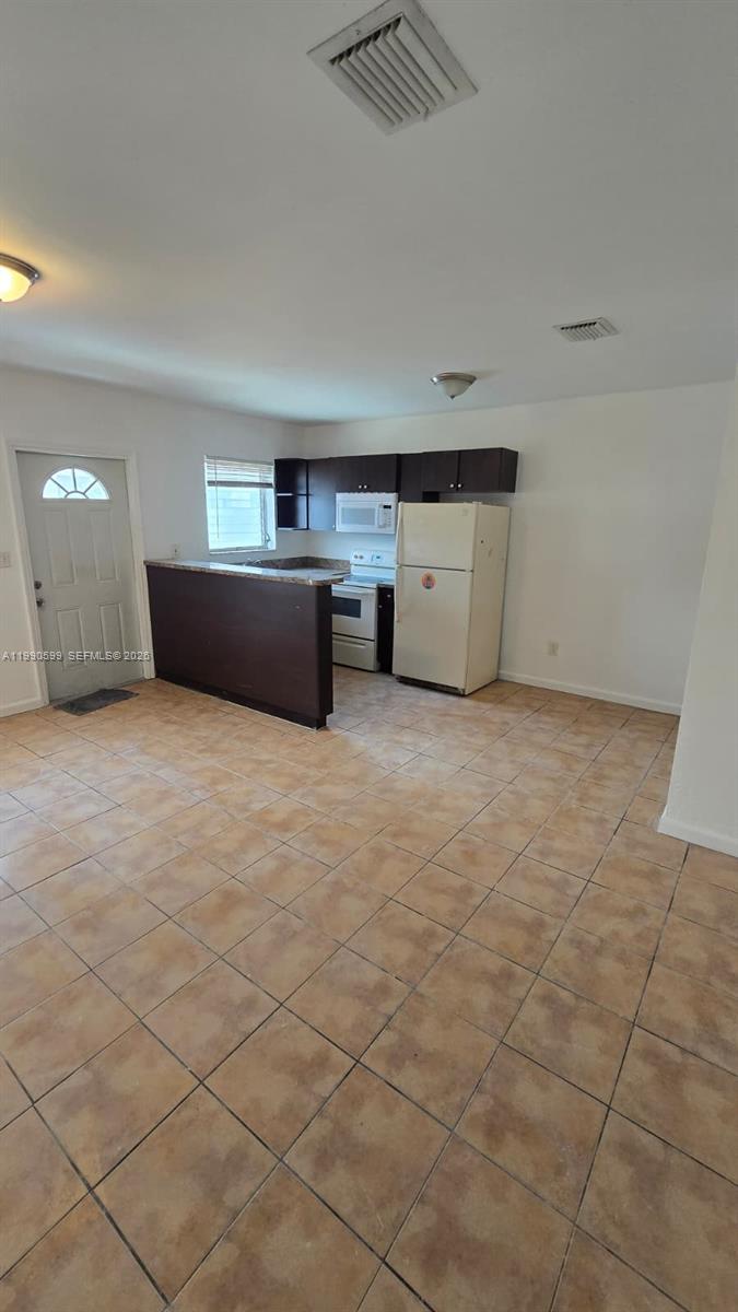 A kitchen with dark cabinets, a breakfast bar, and tile flooring opens into a living area — 16131 NE 19th Pl # 3, North Miami Beach FL 33162, NORTH MIAMI BEACH, FL