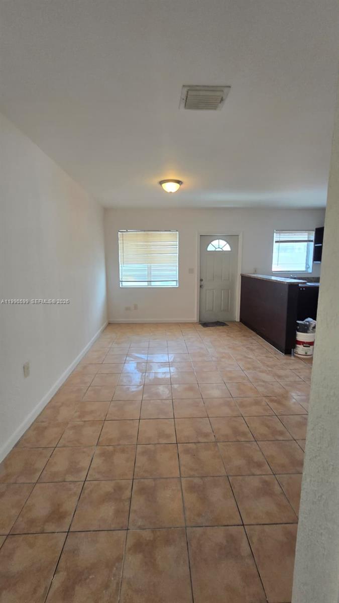 An open-concept room features light-colored tile flooring, a window, a door, and a kitchen counter — 16131 NE 19th Pl # 3, North Miami Beach FL 33162, NORTH MIAMI BEACH, FL