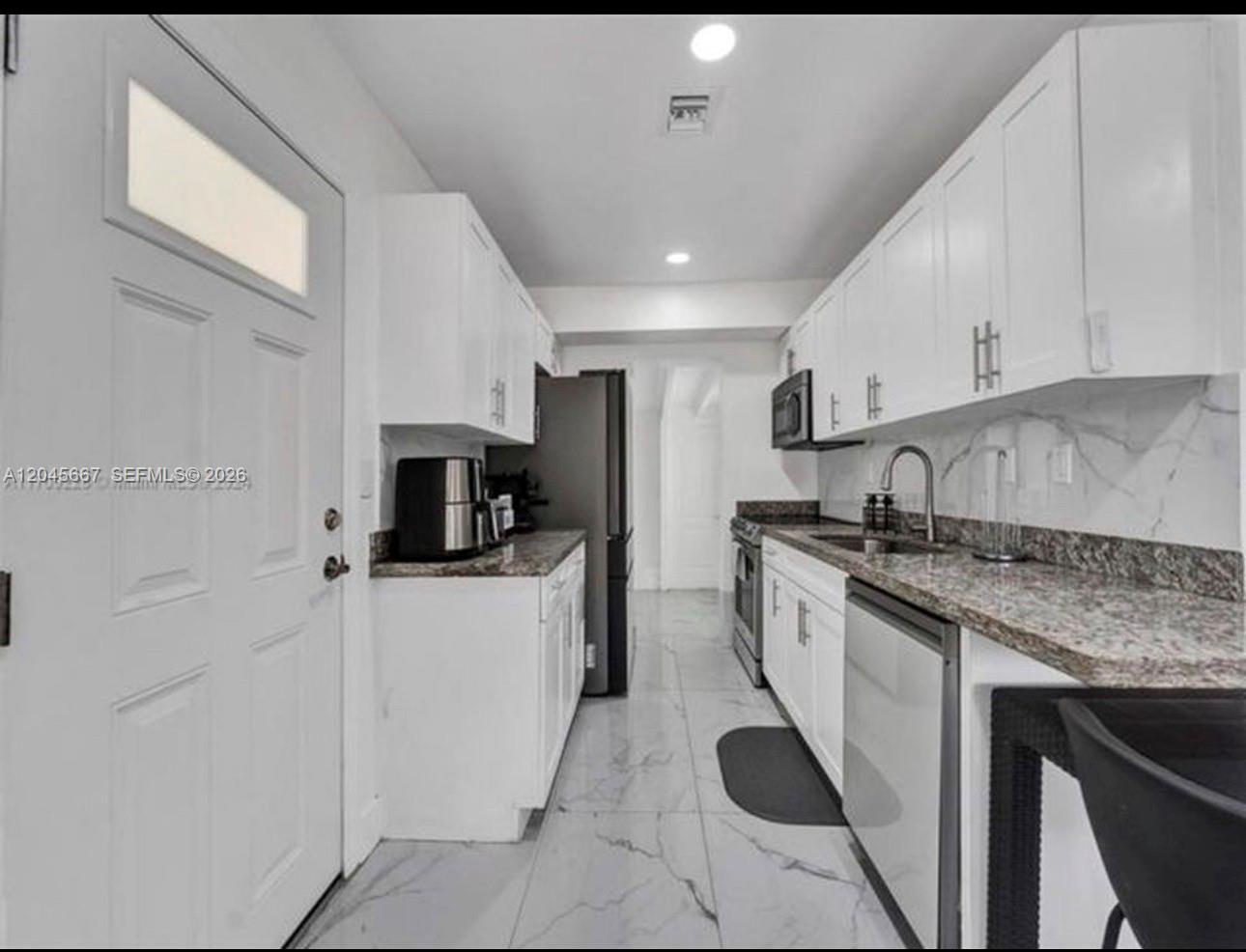 A galley kitchen features white cabinets, granite countertops, stainless steel appliances, and light tile flooring — 2730 NE 16th Ave # 0, Pompano Beach FL 33064, POMPANO BEACH, FL