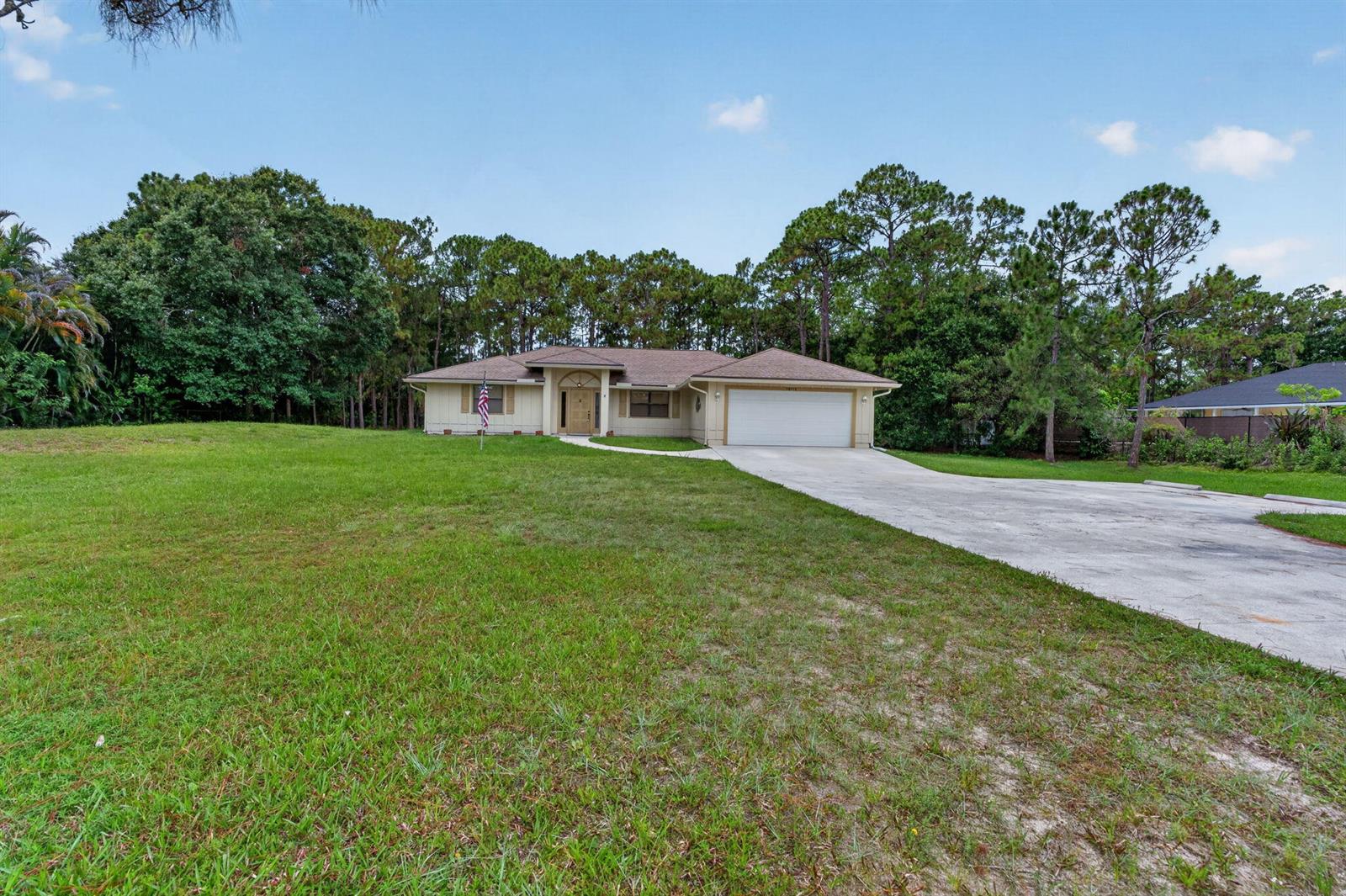 A single-story house with a white garage and a large front lawn sits near trees — 16735 Alexander Run, Jupiter FL 33478, JUPITER, FL