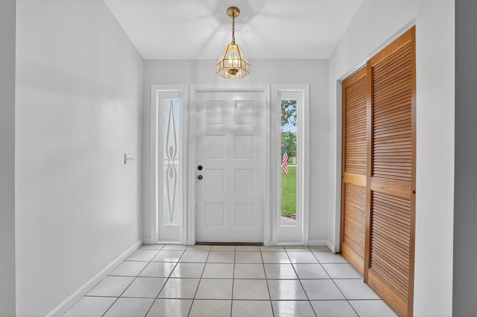 An entryway features white tiled floors, a white front door with sidelights, and wooden closet doors — 16735 Alexander Run, Jupiter FL 33478, JUPITER, FL