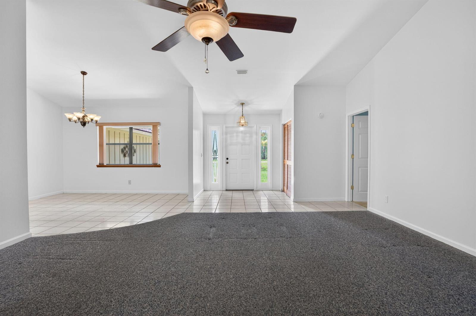 A living room with gray carpet transitions to a tiled entryway and dining area — 16735 Alexander Run, Jupiter FL 33478, JUPITER, FL