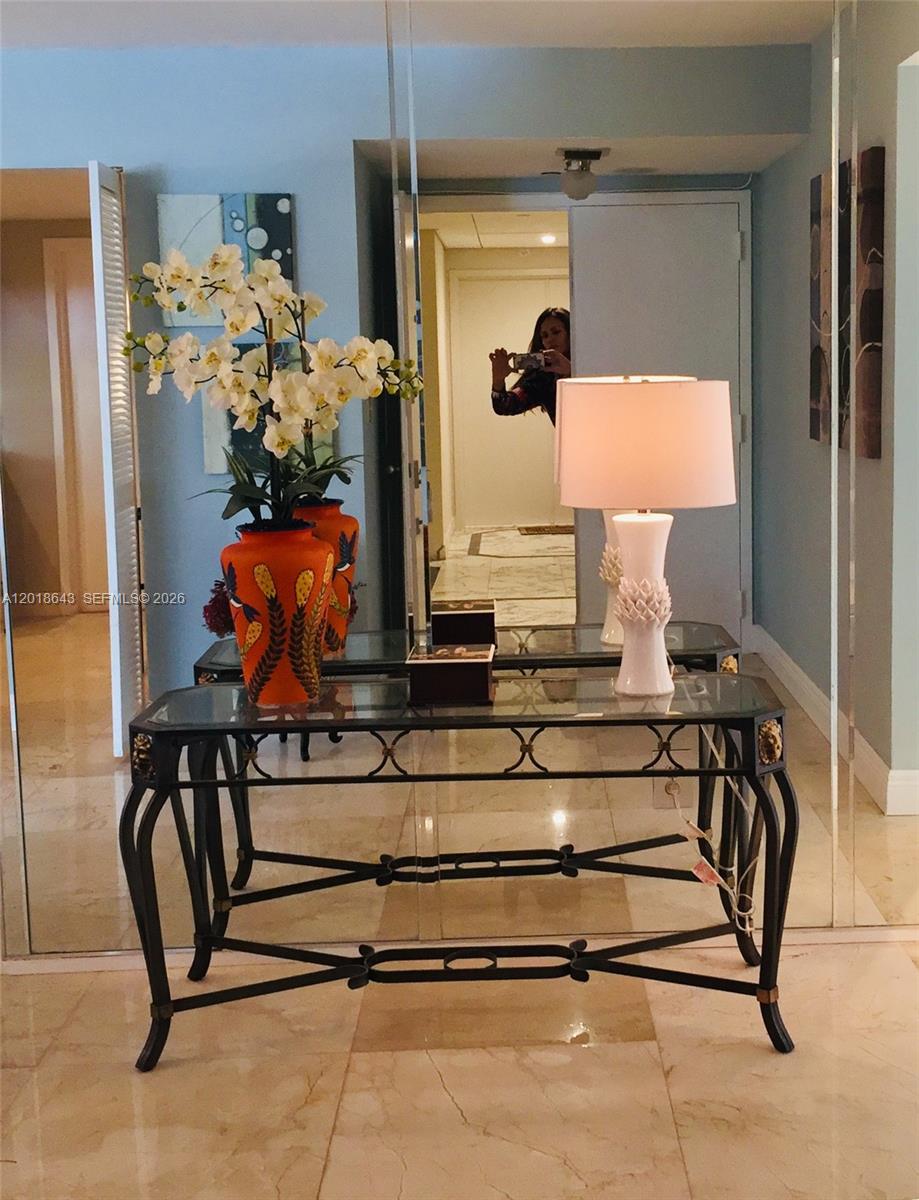 A glass-topped console table with a lamp and floral vase sits before a mirrored wall — 199 Ocean Lane Dr # 113, Key Biscayne FL 33149, KEY BISCAYNE, FL