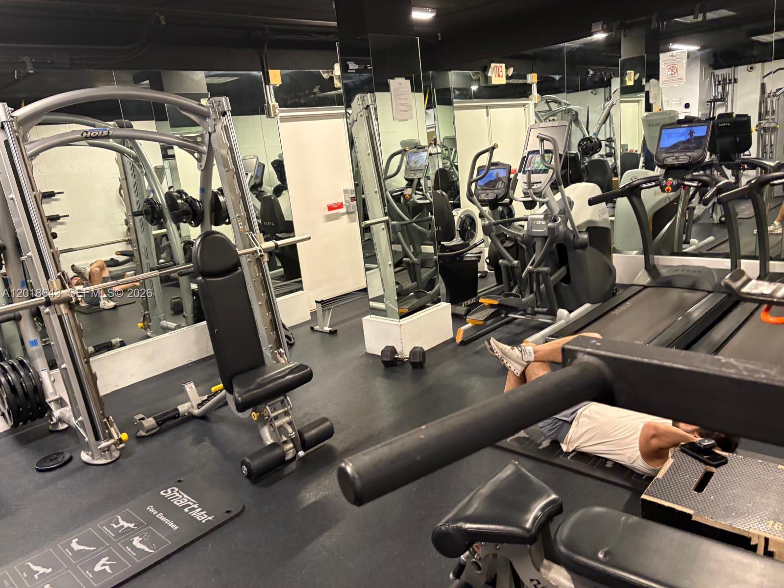 A gym room features a Smith machine, treadmills, and a person exercising on a bench — 199 Ocean Lane Dr # 113, Key Biscayne FL 33149, KEY BISCAYNE, FL
