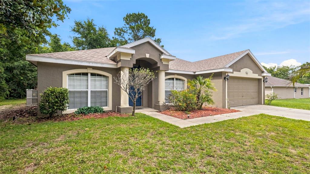 A single-story house with a tan stucco exterior, a two-car garage, and a blue door — 57 PINE DRIVE, HOMOSASSA, FL