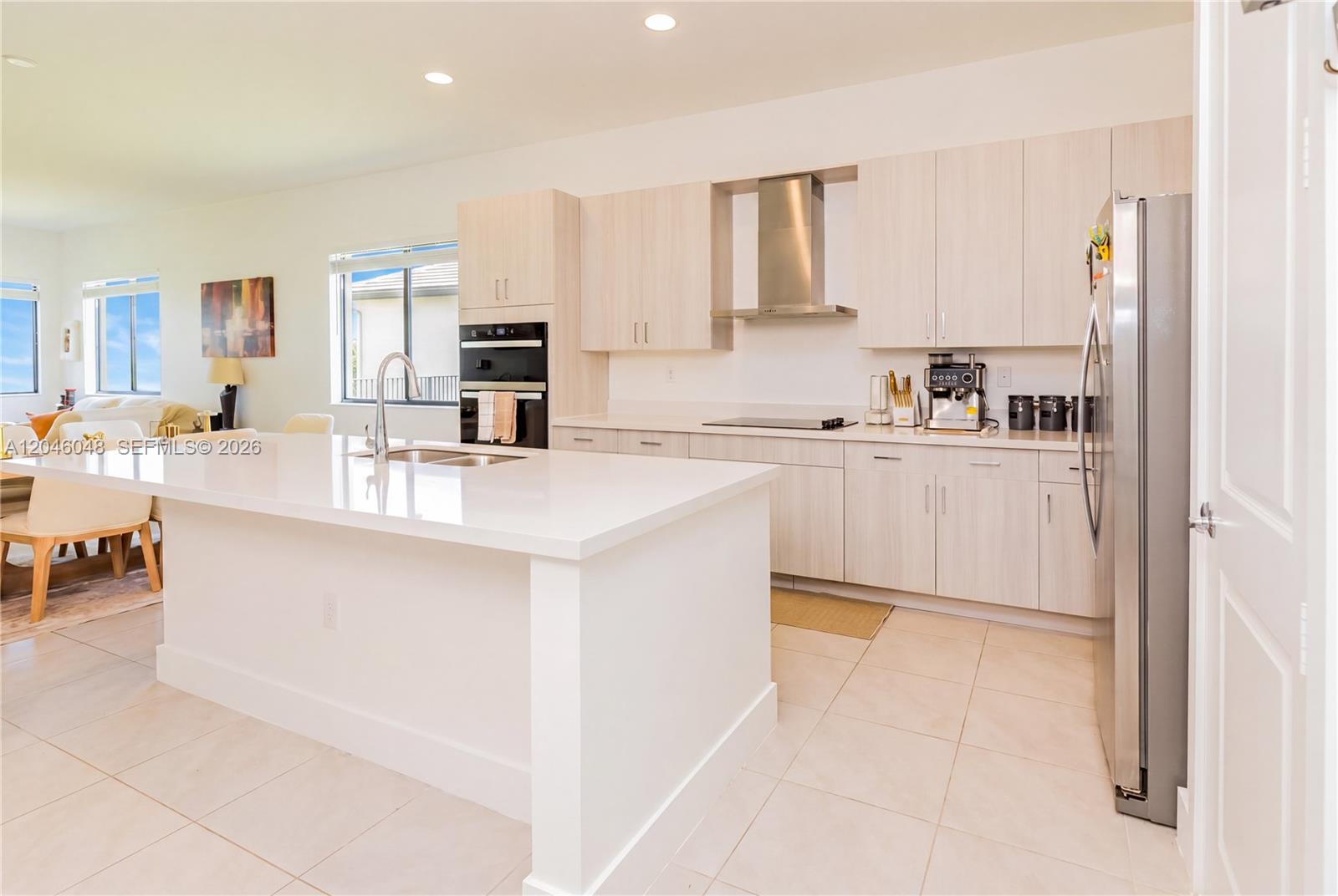 A modern kitchen features light wood cabinets, a white quartz island, and stainless steel appliances — 5261 LAMONE LN, Ave Maria FL 33142, AVE MARIA, FL