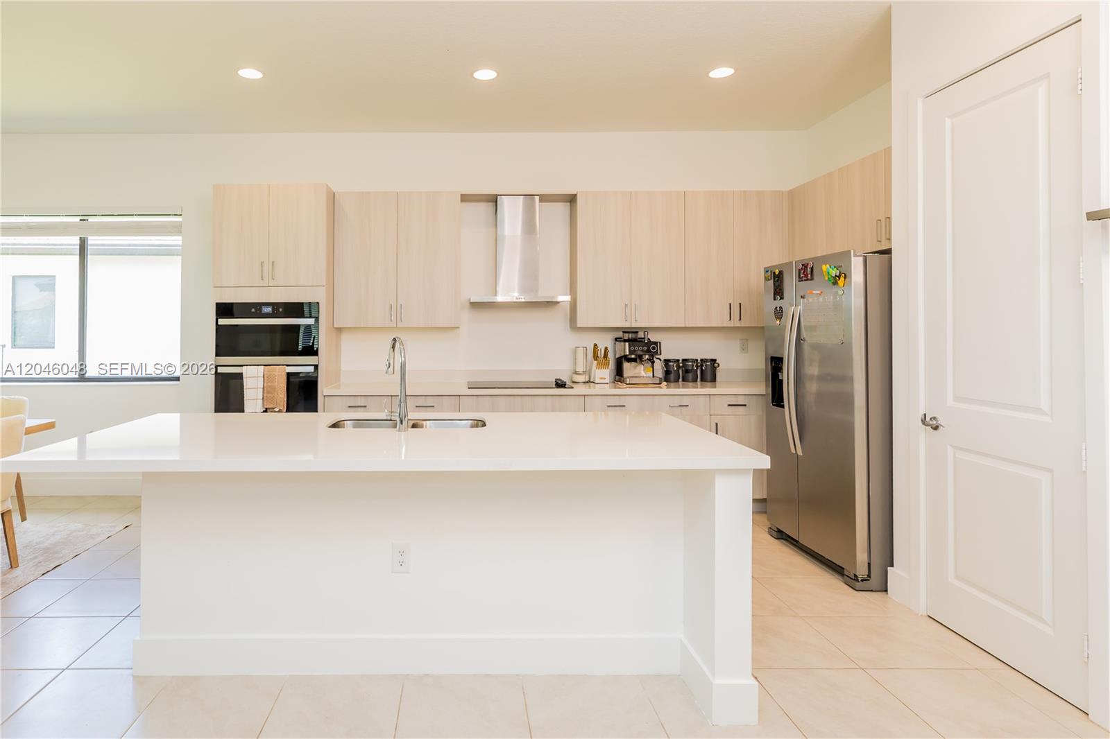 A modern kitchen features light wood cabinets, stainless steel appliances, and a white quartz island — 5261 LAMONE LN, Ave Maria FL 33142, AVE MARIA, FL