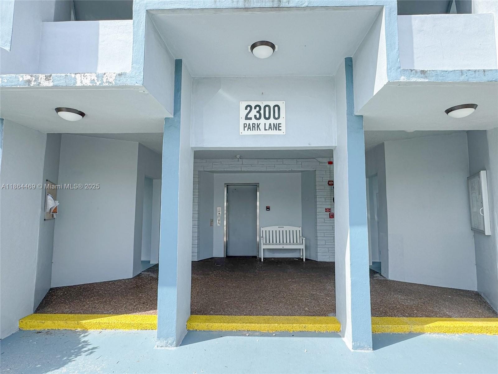 The exterior entrance of a building features a white bench and an elevator door — 2300 Park Ln # 105, Hollywood FL 33021, HOLLYWOOD, FL