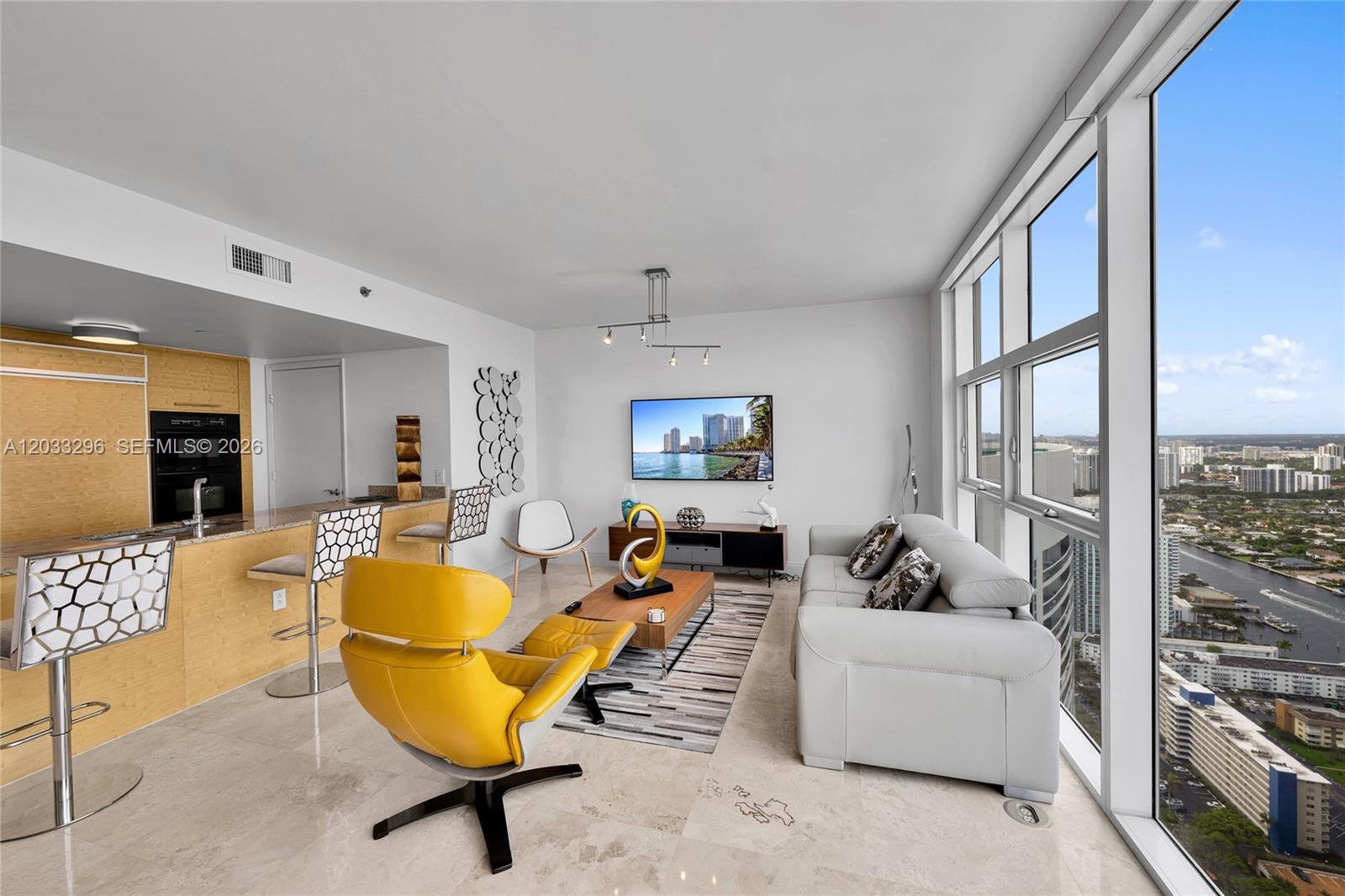 A modern living room with a yellow lounge chair, grey sofa, and floor-to-ceiling windows — 1830 S Ocean Dr # 4807, Hallandale Beach FL 33009, HALLANDALE BEACH, FL
