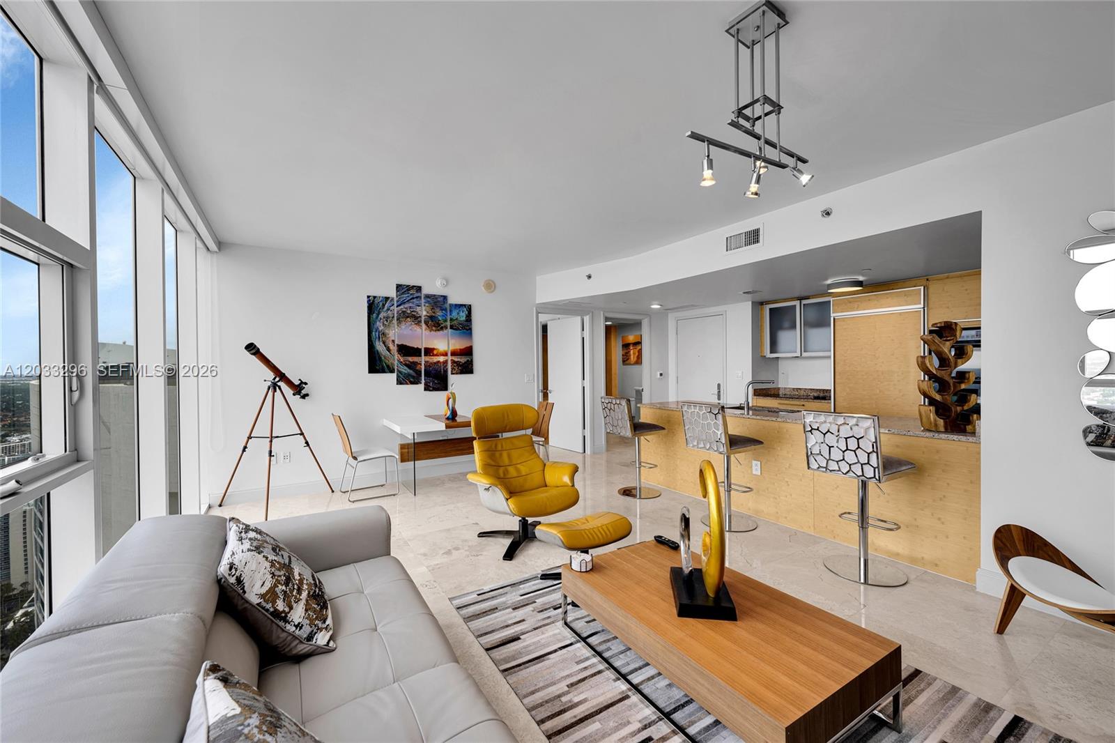 A modern living room features a sofa, yellow lounge chair, kitchen island, and floor-to-ceiling windows — 1830 S Ocean Dr # 4807, Hallandale Beach FL 33009, HALLANDALE BEACH, FL