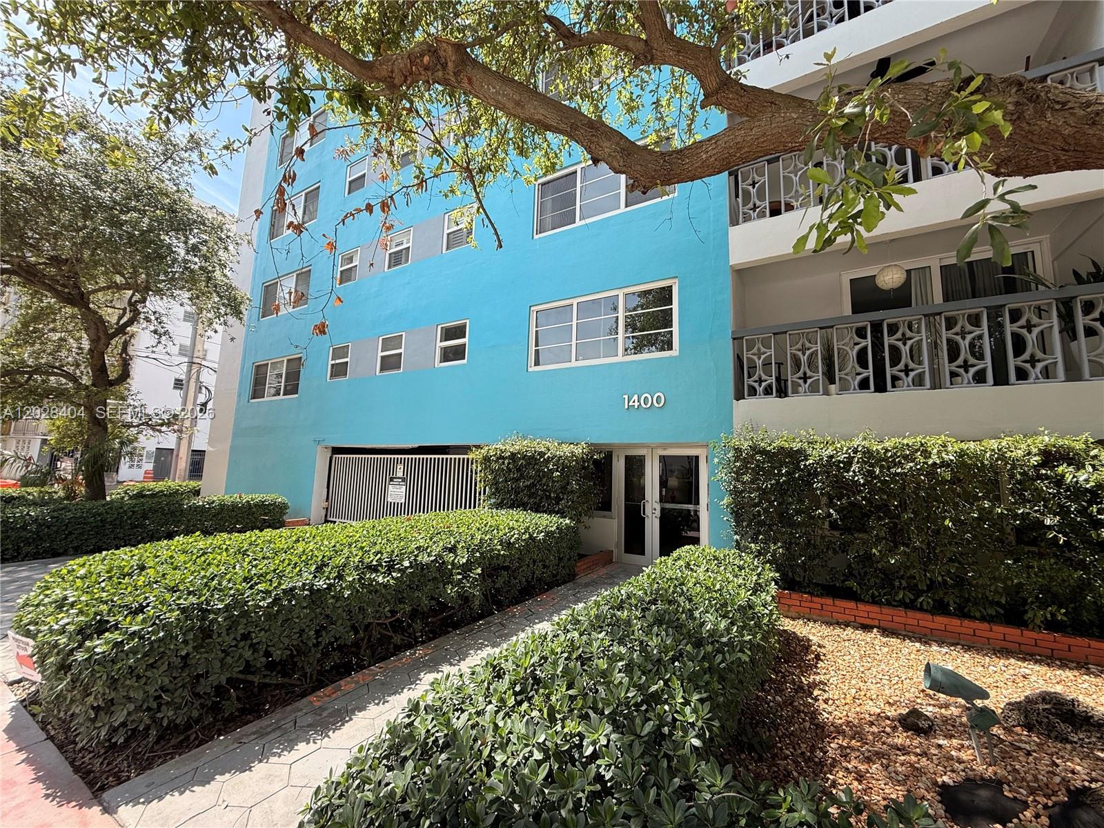 A bright blue multi-story apartment building with a gated entrance and manicured hedges — 1400 Lincoln Rd # 301, Miami Beach FL 33139, MIAMI BEACH, FL