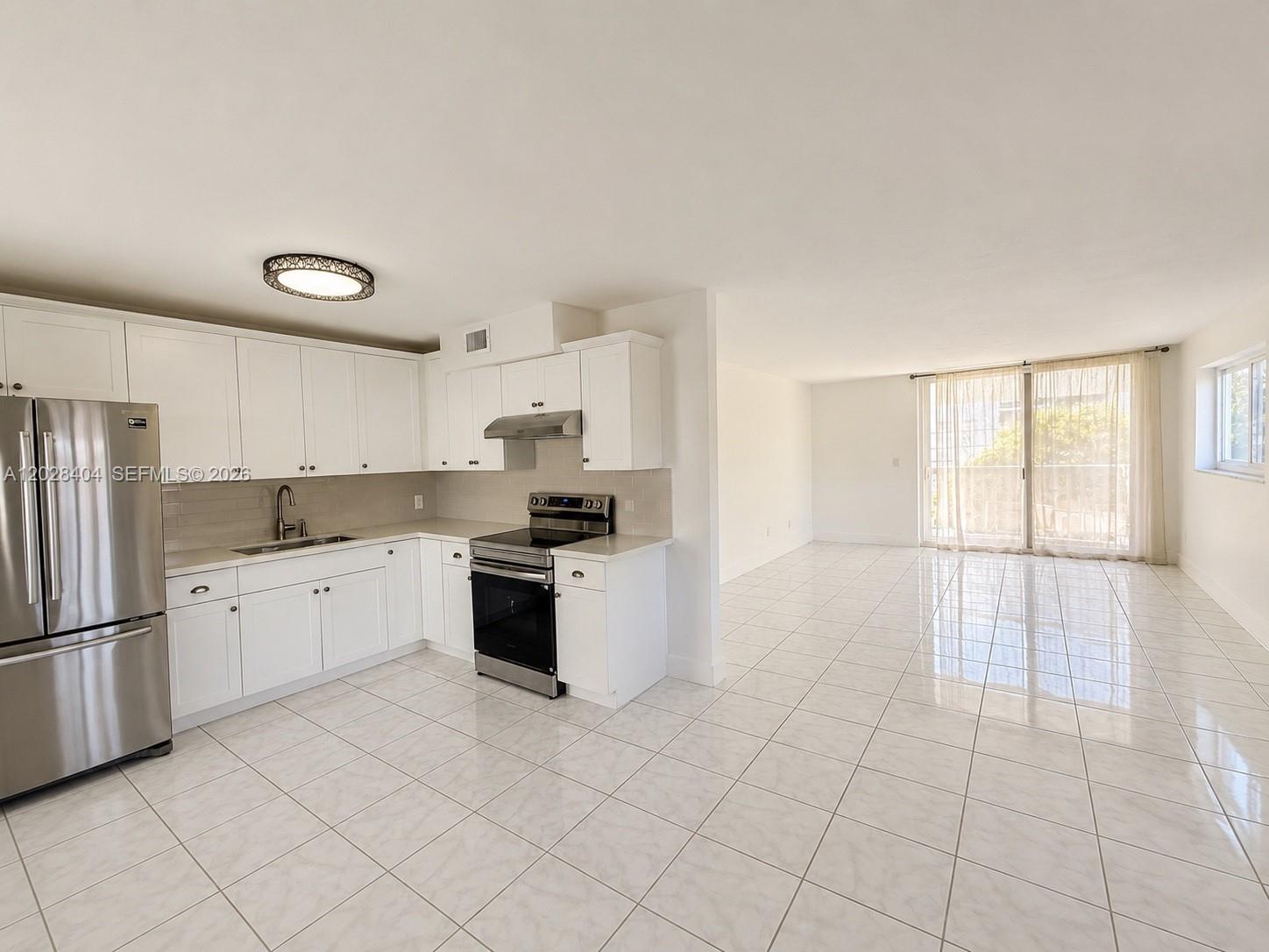 A kitchen with white cabinets and stainless steel appliances opens to a tiled living area — 1400 Lincoln Rd # 301, Miami Beach FL 33139, MIAMI BEACH, FL