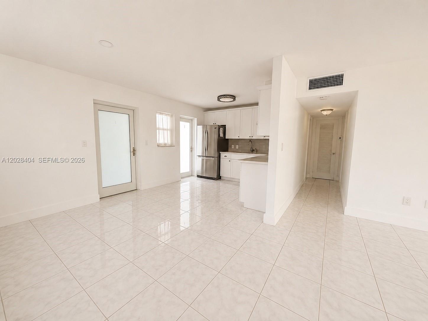 A kitchen with white cabinets and stainless steel appliances opens into a tiled living area — 1400 Lincoln Rd # 301, Miami Beach FL 33139, MIAMI BEACH, FL